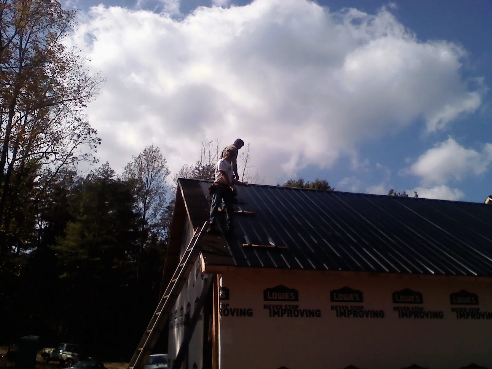 Roofer fastening dark metal panels high against a cloudy sky, from a Roof Inspection job in Mesa